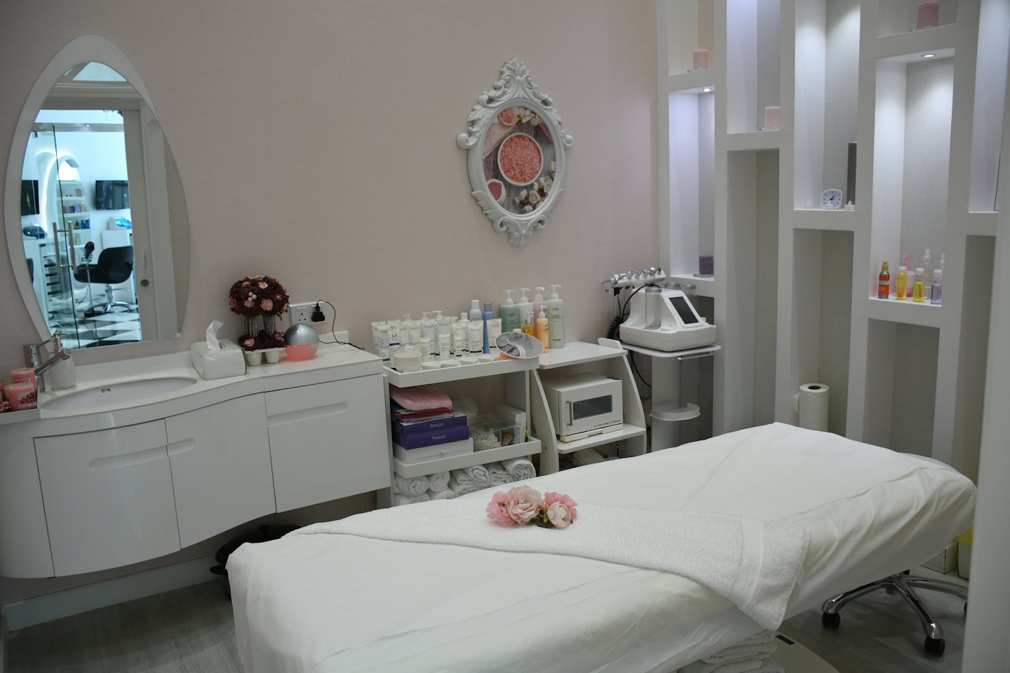 Clean beauty salon treatment room with white bed and pink flowers.