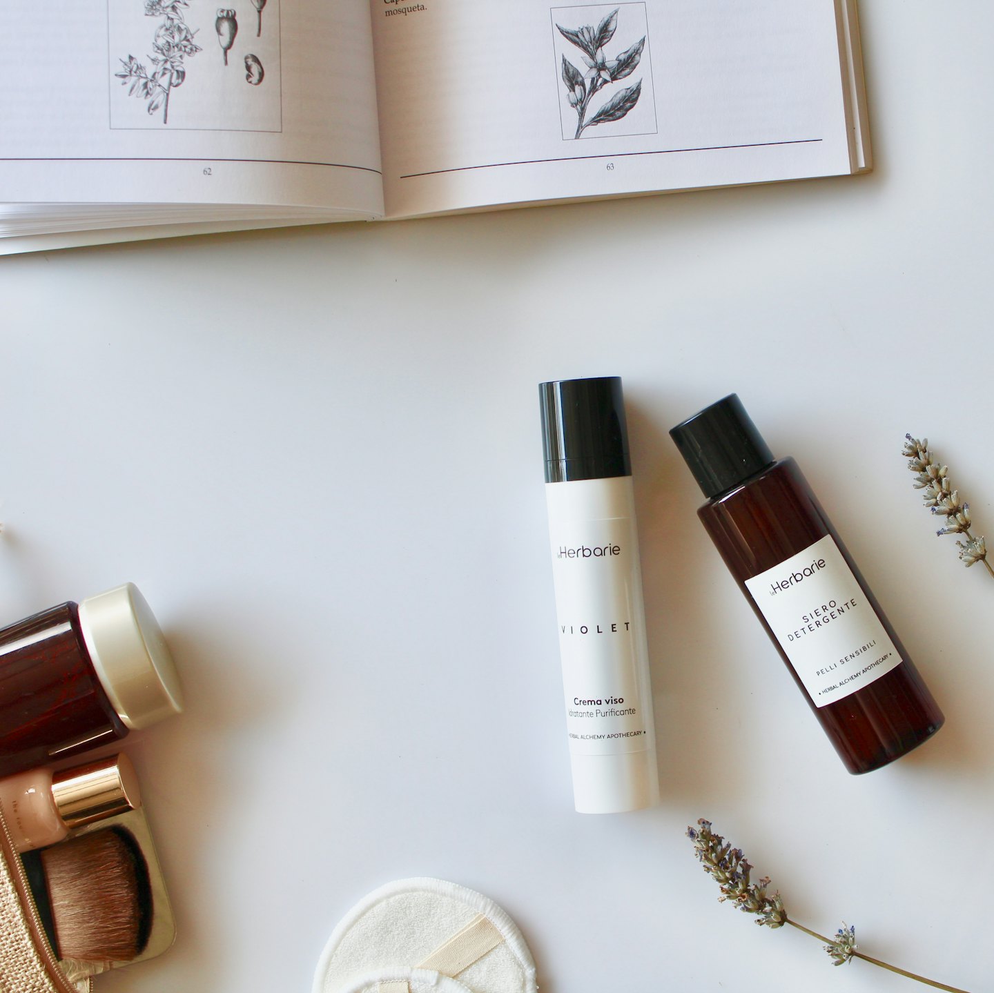 Herbarie skincare bottles with botanical book and lavender sprigs.